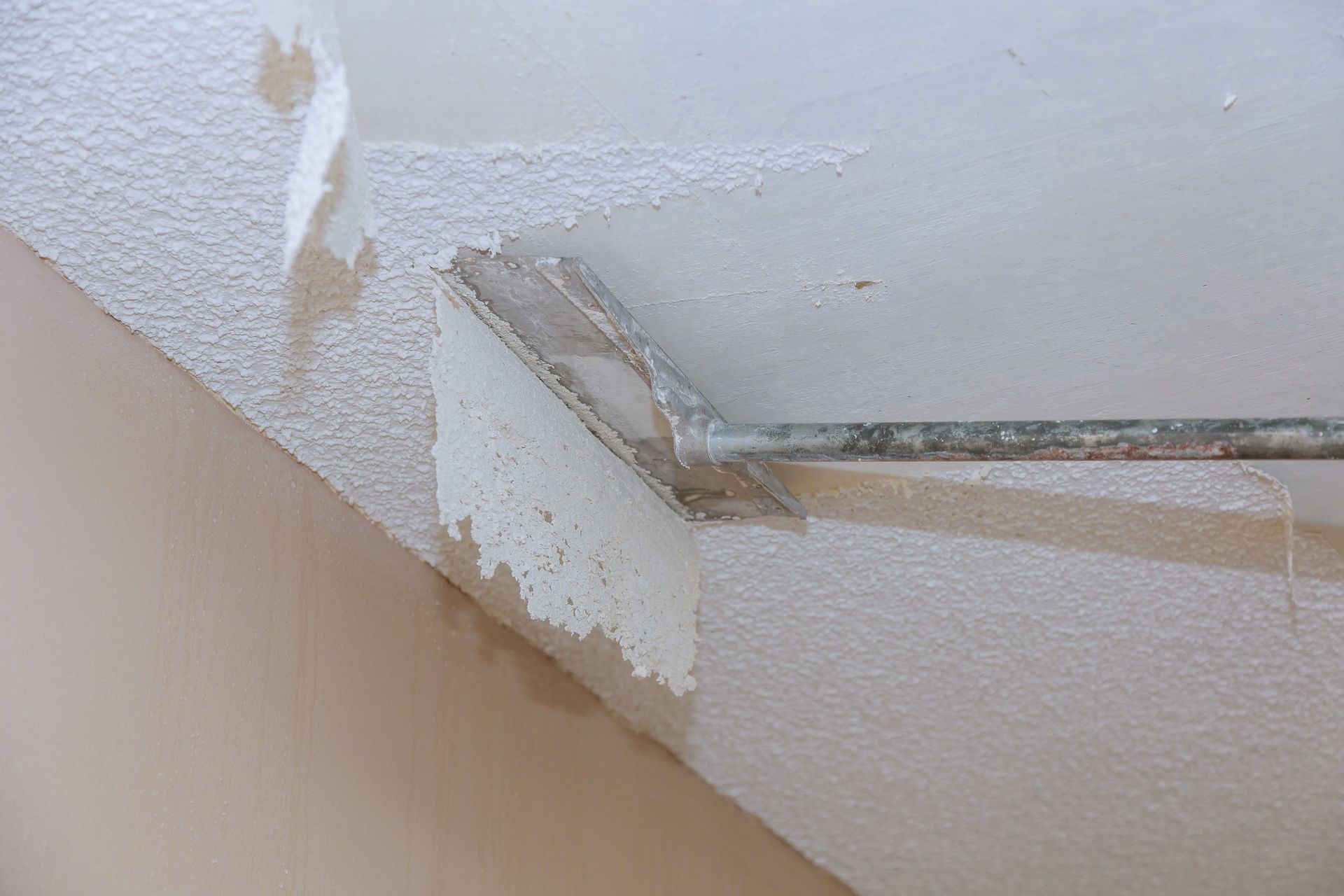 Removing popcorn ceiling texture with scraper